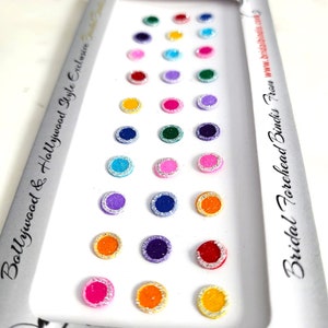 May include: A sheet of 20 colourful, round, self-adhesive bindi stickers with silver glitter trim. The bindi stickers are arranged in rows on a white background. The text "Bridal Forehead Bindis Row" and "www.bridalbindis.com" are printed on the white background.