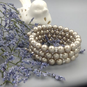 May include: A multi-strand bracelet made of beige pearls with rhinestone accents. The bracelet is wrapped around a white ceramic bird figurine.