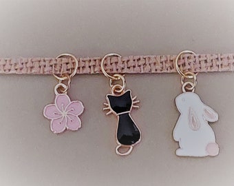 May include: A brown woven cord with three charms: a pink flower, a black cat, and a white rabbit.