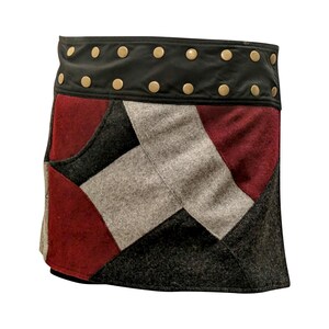May include: A patchwork mini skirt featuring a black leather waistband with gold-colored studs. The skirt's design incorporates geometric shapes in shades of red, gray, and black. The skirt is a unique piece of clothing.
