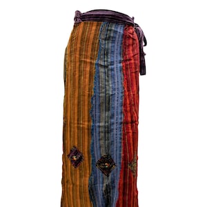Op de afbeelding: Een lange, veelkleurige wikkelrok met een gestreept patroon in tinten oranje, rood, blauw en bruin. De rok heeft een decoratieve zoom en geborduurde details.