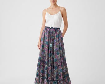 May include: A white camisole with thin straps paired with a floor-length, tiered maxi skirt featuring a dark blue, purple, and teal floral paisley pattern, a gathered elastic waistband with a drawstring, and a ruffled hemline.