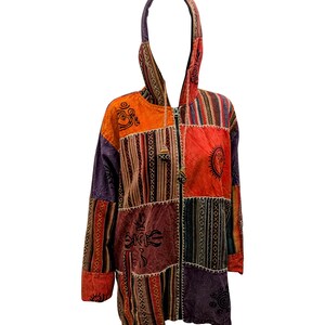May include: A multi-coloured patchwork hooded jacket with a zip closure. The jacket features a variety of patterns, including stripes, geometric designs, and symbols. The hood is lined with a purple fabric.