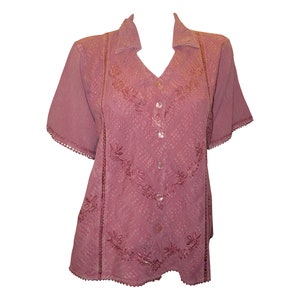 May include: A mauve button-up shirt with short sleeves and a scalloped trim. The shirt has a V-neck and is decorated with embroidered floral designs.