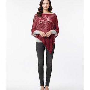 May include: A burgundy open-weave poncho with a square neckline. The poncho is worn over a grey long-sleeved top and dark grey jeans. The person is also wearing black heels. The background is white.