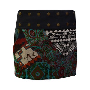 Könnte beinhalten: Ein kurzer, mehrfarbiger Rock mit Patchwork-Design, das geometrische und Paisley-Muster zeigt. Der Rock hat einen dunkelblauen Bund mit dekorativen Metallnieten.