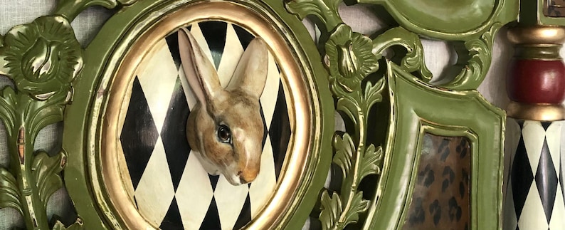 May include: A decorative wall hanging featuring a rabbit head emerging from a circular frame with a black and white diamond pattern. The frame is gold-trimmed and set within a larger, ornate green frame with floral accents.