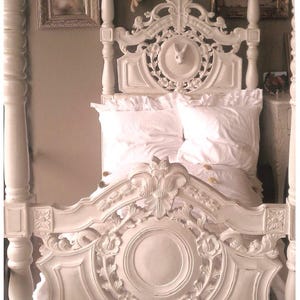 May include: White wooden bed frame with intricate carvings and a carved rabbit head in the headboard. The bed is made up with white bedding.