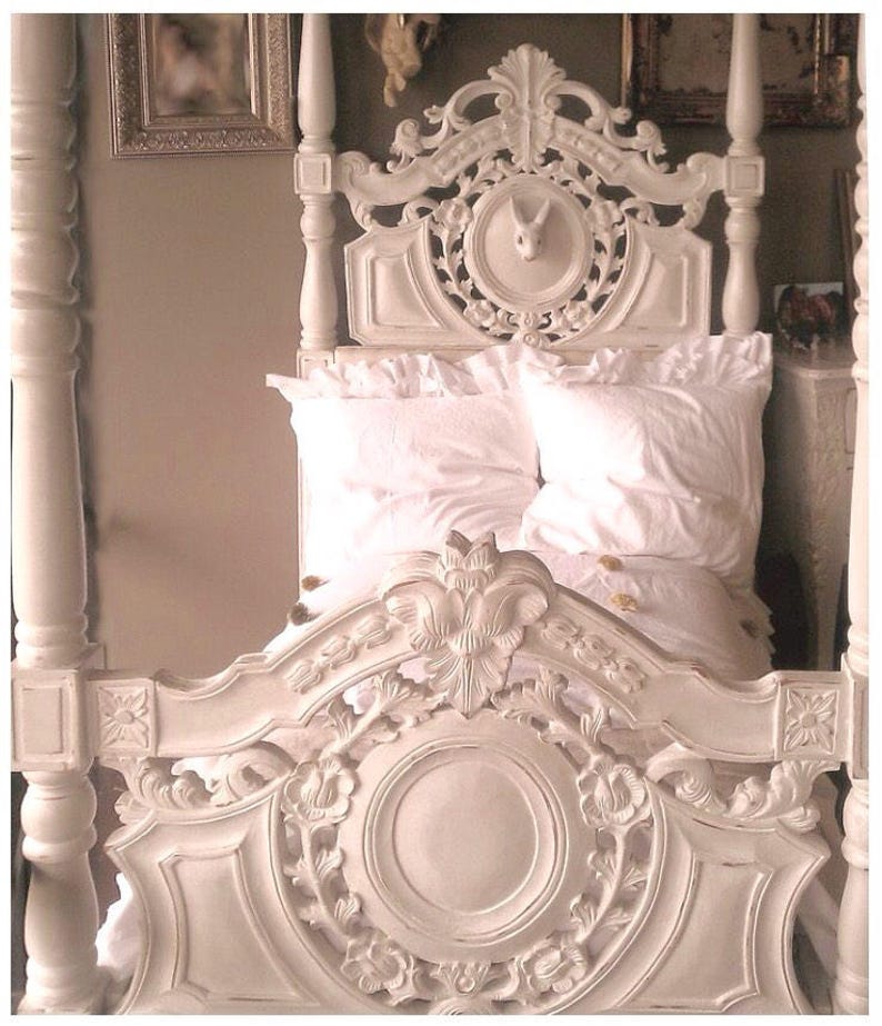 May include: White wooden bed frame with intricate carvings and a carved rabbit head in the headboard. The bed is made up with white bedding.