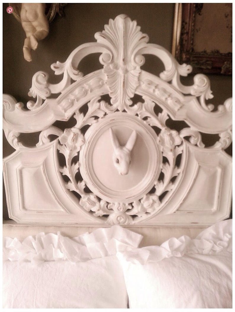 May include: White ornate headboard with a carved rabbit head in the center. The headboard is made of wood and has a distressed white finish.