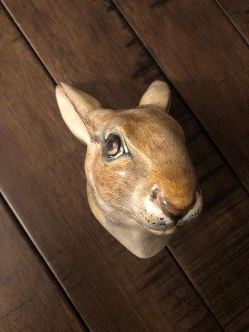 May include: A ceramic rabbit head sculpture with brown and white fur, painted details, and black eyes.