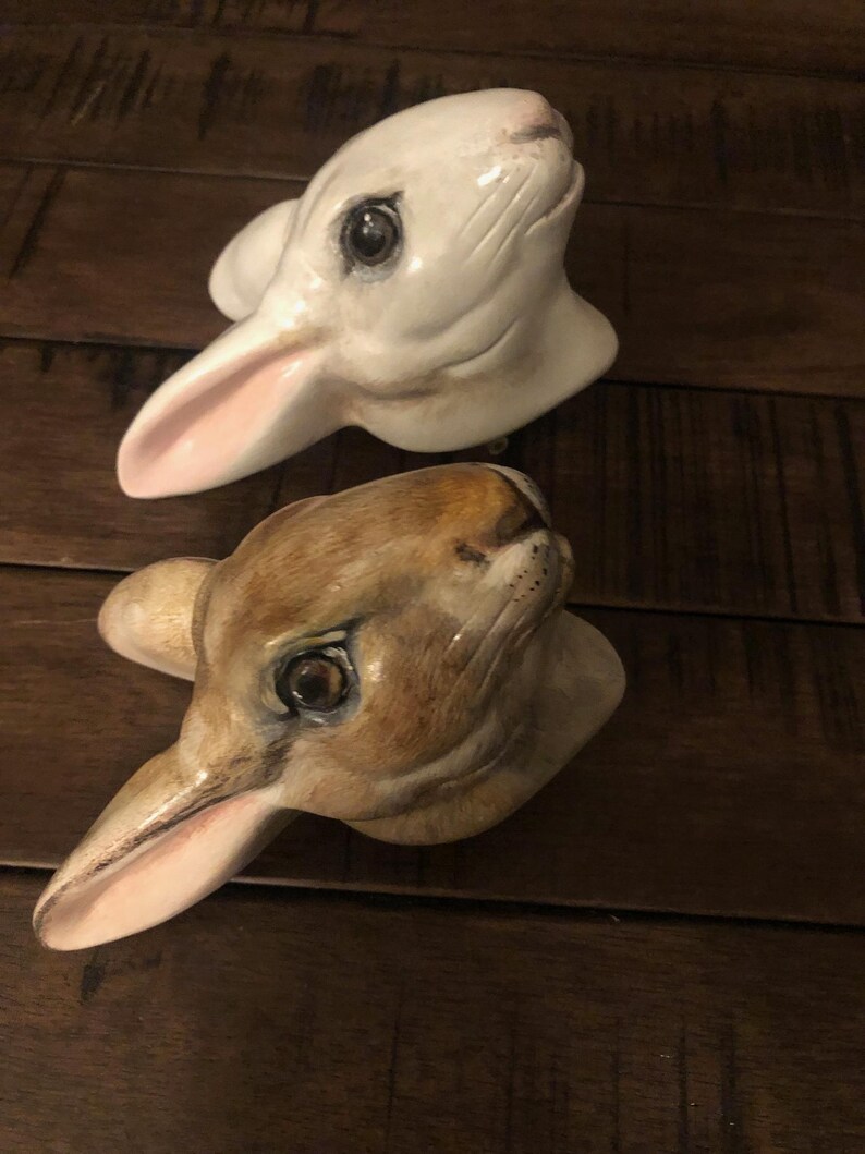 May include: Two ceramic rabbit heads, one white with pink ears and one brown with pink ears. Both have realistic details and painted eyes.