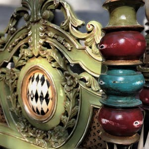 May include: Close-up of a decorative, ornate headboard and bed post. The headboard is painted green with gold accents and a patterned center. The bed post is painted with red, green, and teal sections.