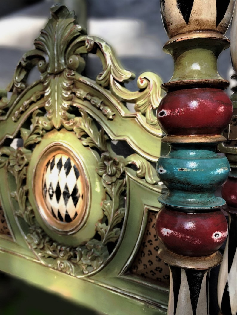 May include: Close-up of a decorative, ornate headboard and bed post. The headboard is painted green with gold accents and a patterned center. The bed post is painted with red, green, and teal sections.