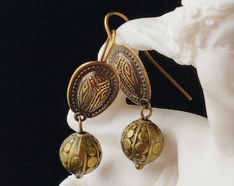 May include: A pair of gold-toned dangle earrings with a round, textured bead and a decorative, oval-shaped charm.