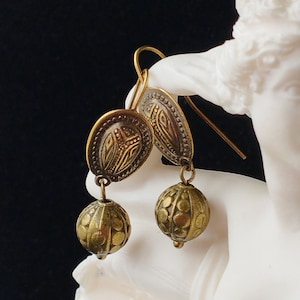 May include: A pair of gold-toned dangle earrings with a round, textured bead and a decorative, oval-shaped charm.