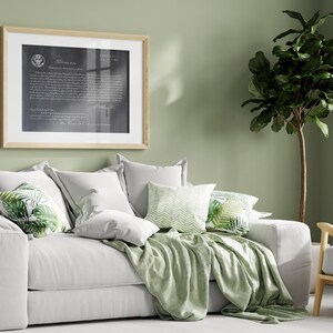 May include: A white sofa with a green throw blanket and pillows with a tropical leaf pattern. The sofa is in a room with a green wall and a large potted plant.