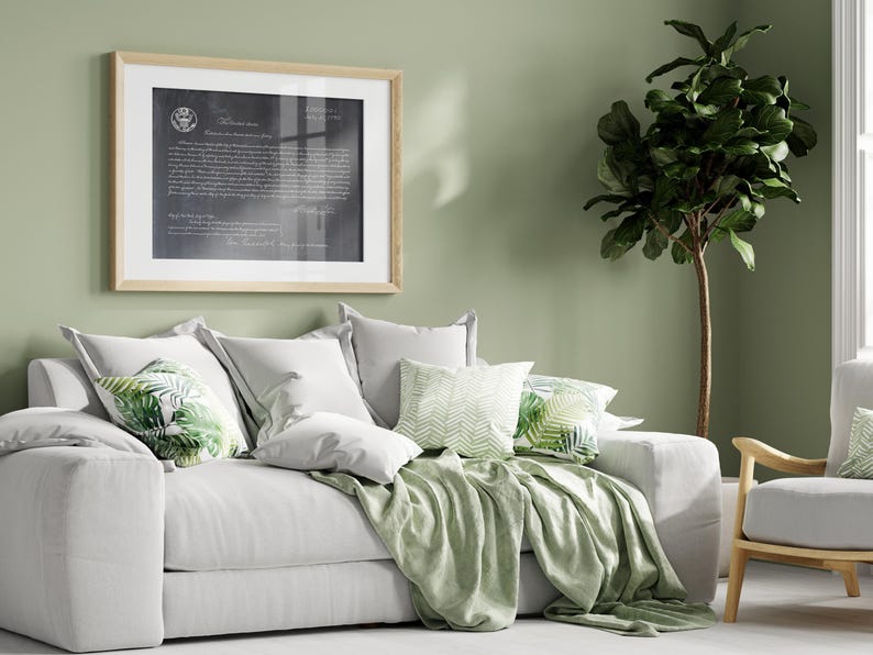 May include: A white sofa with a green throw blanket and pillows with a tropical leaf pattern. The sofa is in a room with a green wall and a large potted plant.