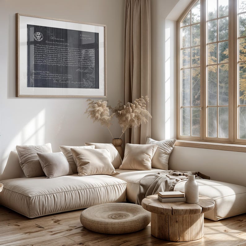 May include: A beige sectional sofa with multiple pillows, a wooden coffee table, and a vase with dried flowers in the background. The sofa is in a living room with a large window and beige curtains.
