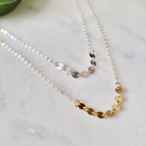 May include: Two delicate necklaces with a layered design. The top necklace features a silver chain with small silver circles, while the bottom necklace has a gold chain with small gold circles.