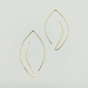 May include: A pair of gold leaf-shaped earrings. The earrings are made of thin wire and have a simple, minimalist design.