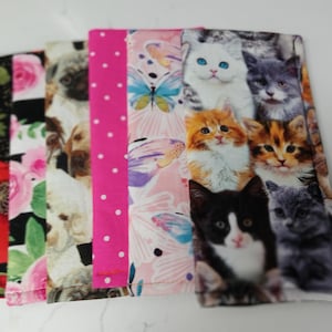 May include: A collection of fabric items with various patterns. Designs include red poppies, pink roses, dog portraits, pink polka dots, butterflies, and cat faces. The items are arranged side by side.