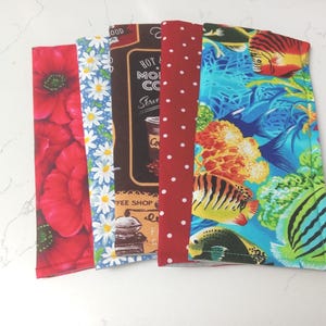 May include: Five rectangular fabric covers arranged side-by-side. The patterns include red poppies, white daisies on blue, a brown coffee shop theme with text, red with white polka dots, and a vibrant underwater scene with tropical fish and coral.