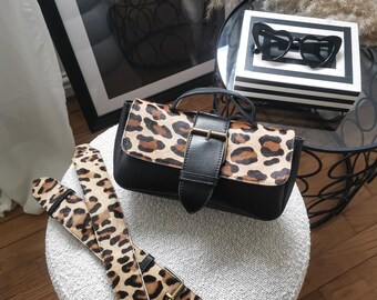 May include: A small black and leopard print handbag with a gold buckle and a matching leopard print strap.
