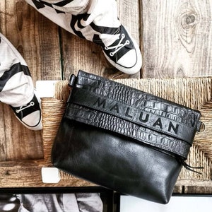 Peut inclure: Sac à bandoulière en cuir noir avec une texture en relief de crocodile et une bandoulière noire avec le mot "MALUAN" imprimé dessus.