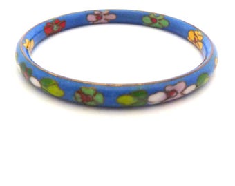 May include: A thin, circular bangle bracelet featuring a vibrant blue enamel base decorated with a repeating pattern of small, multi-colored flowers in shades of red, yellow, pink, white, and green, finished with a metallic edge.