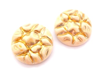 May include: Two gold-colored, round earrings with a textured, raised design. The earrings have a light peach base color with gold accents, and are set against a white background. The earrings are likely vintage or costume jewelry.