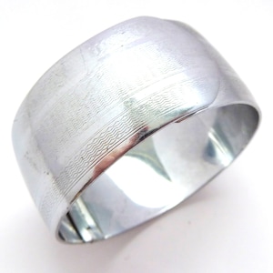 Puede incluir: Un brazalete de metal plateado con un diseño texturizado. El brazalete está abierto y tiene un cierre con bisagra.