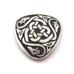 May include: A silver-colored, triangular guitar pick with a Celtic knot design. The pick features a detailed, interwoven pattern of lines and shapes, with a raised border. The design includes stylized dragon heads.