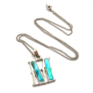 Op de afbeelding: Een zilveren ketting met een hanger in de vorm van de letter "M". De hanger is gemaakt van zilver en heeft een blauwe en groene abalone-schelp inlay.