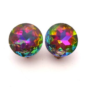May include: A pair of round stud earrings featuring faceted, iridescent glass stones that display a vibrant spectrum of colors including magenta, green, yellow, and blue. The stones have a star-shaped pattern cut into the surface, creating a reflective, multi-colored effect.