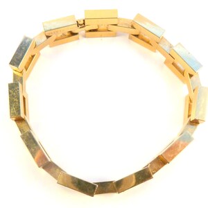 May include: A gold-colored bracelet made of interlocking rectangular links. The bracelet is open and laid flat on a white surface.
