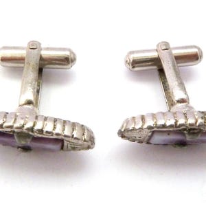 Pu&ograve; includere: Un paio di gemelli d'argento con un'intarsio di madreperla di abalone viola. I gemelli hanno un design decorativo attorno alla conchiglia.