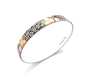 May include: A round bangle bracelet featuring a patterned exterior with black, white, and peach-colored floral and dotted motifs. The interior of the bracelet is white and displays the signature text Michaela Frey in black script lettering.