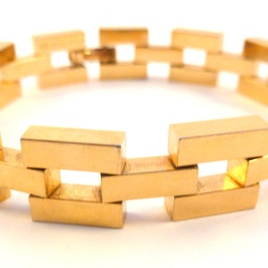 May include: A gold-colored bracelet with a linked chain design. The bracelet is made of rectangular links that are connected to each other in a repeating pattern.