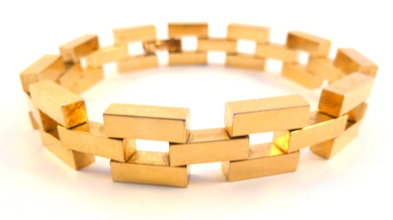May include: A gold-colored bracelet with a linked chain design. The bracelet is made of rectangular links that are connected to each other in a repeating pattern.