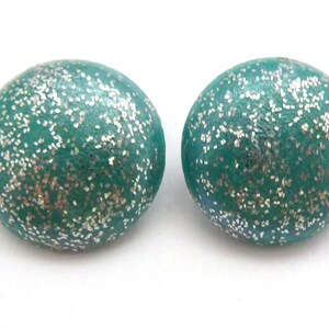 Op de afbeelding: Een paar ronde oorbellen in tealblauw met zilveren glitter ingebed in het oppervlak.