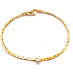 Könnte beinhalten: Ein goldenes Kettenarmband mit einem einzigen klaren Stein in der Mitte.