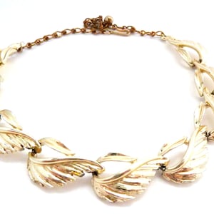 May include: A gold-tone necklace featuring a chain and a design of stylised leaves. The leaves are textured and have a slightly raised design.