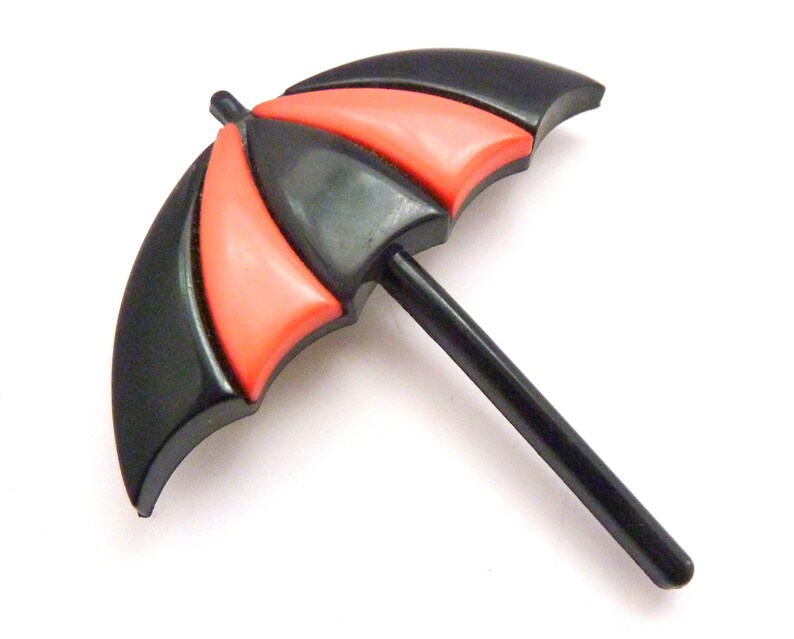 May include: A black and red plastic umbrella brooch. The umbrella is closed and has a black handle.
