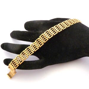 Puede incluir: Una pulsera de metal en tono dorado con un diseño de eslabones repetitivos en forma de escalera y barras horizontales texturizadas. La pulsera cuenta con un mecanismo de cierre rectangular en un extremo y eslabones calados.