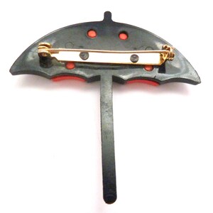 May include: Black and red umbrella brooch with a gold pin. The umbrella has a black handle and red accents.