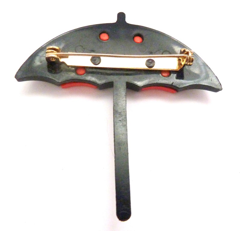 May include: Black and red umbrella brooch with a gold pin. The umbrella has a black handle and red accents.