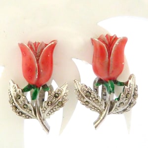 Peut inclure: Une paire de boucles d'oreilles à clip vintage représentant des boutons de roses rouges avec des tiges vertes et des feuilles argentées. Les boucles d'oreilles ont un design détaillé et texturé, sur le thème floral.