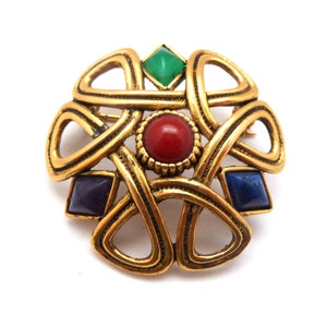 May include: Gold-toned brooch with an intricate design featuring four gemstones: a red, a green, a blue, and a purple.