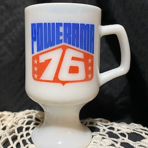 May include: White ceramic mug with a blue and red Powerama 76 logo. The mug has a pedestal base.
